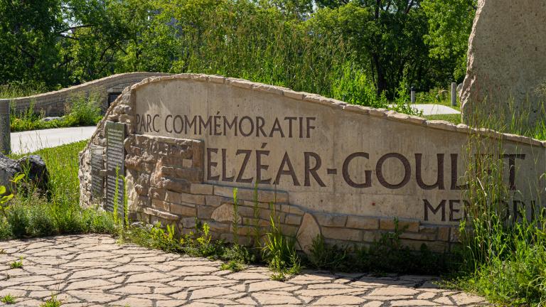 Sculpture de roche et de maçonnerie en forme de mur incurvé sur lequel est inscrit en gros caractères « Parc commémoratif Elzéar Goulet ».