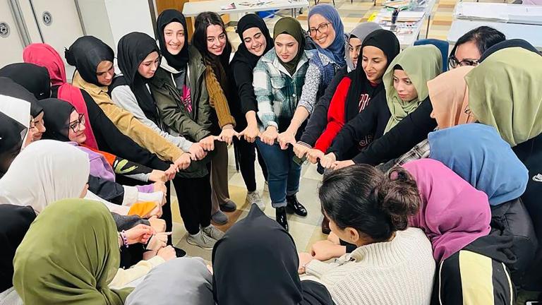 Un groupe de femmes musulmanes souriantes formant un cercle et se tenant par la main. Visibilité masquée.