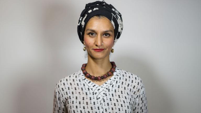 Une femme pakistanaise, Anna Abbas, portant un bandeau noir et blanc, un rouge à lèvres rouge, un collier brun épais et un chemisier noir et blanc regarde vers l'avant d'un air perplexe. Visibilité masquée.
