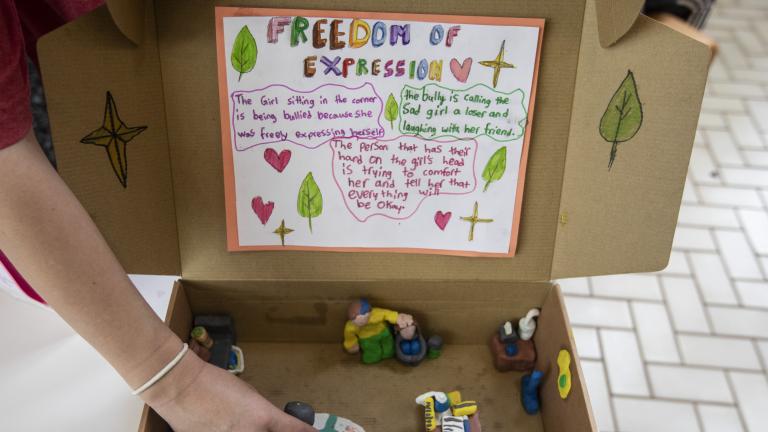 Une boîte en carton ouverte contenant une scène représentant des personnes en interaction, réalisée en argile. 