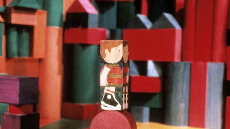 Un bloc de bois, sur lequel est peinte l'image d'un enfant, est posé sur un bloc rond. Des blocs de formes, de couleurs et de tailles différentes apparaissent à l'arrière-plan.