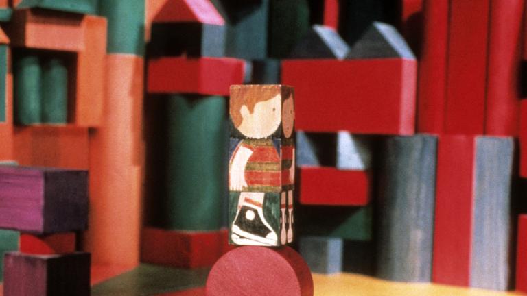 Un bloc de bois, sur lequel est peinte l'image d'un enfant, est posé sur un bloc rond. Des blocs de formes, de couleurs et de tailles différentes apparaissent à l'arrière-plan. Visibilité masquée.