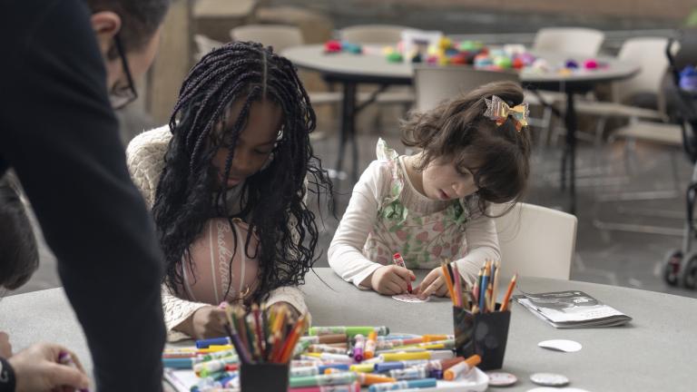 Deux jeunes enfants sont assis côte à côte à une table ronde, occupés à une activité artistique avec des marqueurs et des crayons de couleur. Visibilité masquée.