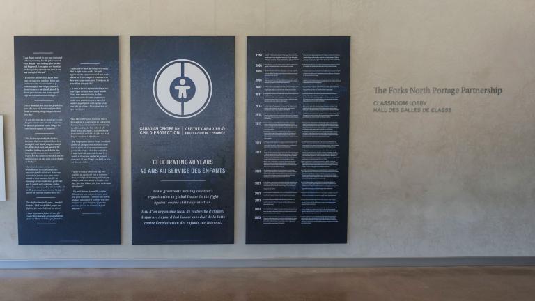 Grands panneaux bleu foncé avec texte et graphiques blancs exposés dans le Corridor communautaire du Musée canadien pour les droits de la personne. Le panneau central comporte un logo circulaire et commémore le 40e anniversaire du Centre canadien de protection de l'enfance. Les deux panneaux de chaque côté présentent du texte bilingue en anglais et en français. Visibilité masquée.