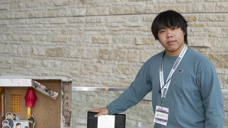 Un jeune homme se tient à côté d’une maquette ressemblant à un restaurant chinois. Un côté est bien rangé et comporte des illustrations de personnes en train de manger. L’autre côté est vide et endommagé.