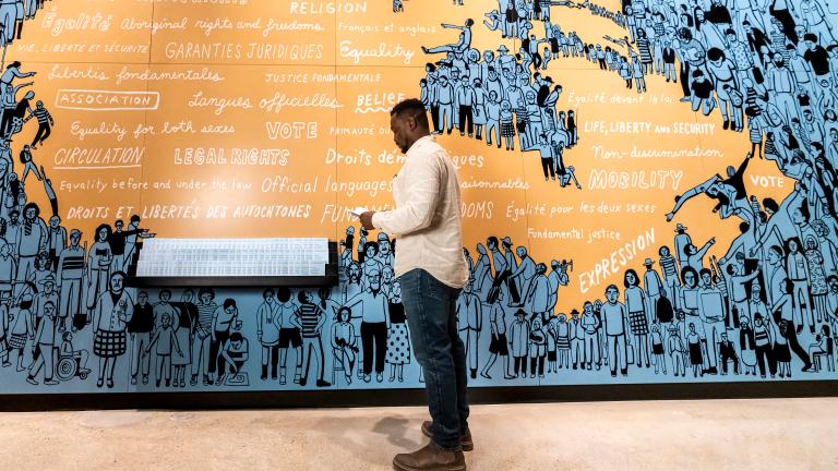 Un homme se tient devant une carte du Canada illustrée en bleu et orange. Visibilité masquée.