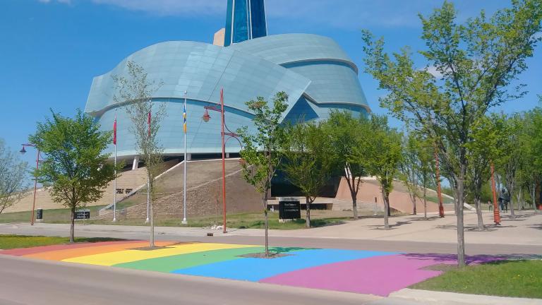 A rainbow crosswalk in front of the Canadian Museum for Human Rights on a sunny day Visibilité masquée.