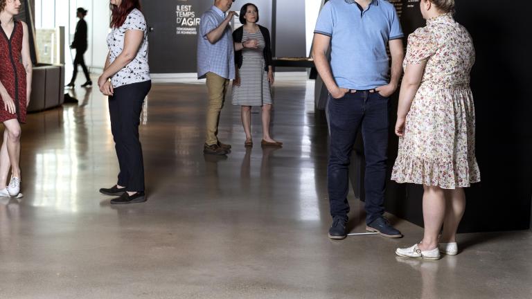 Des petits groupes de personnes en conversation debout dans un espace d’exposition de Musée. Visibilité masquée.