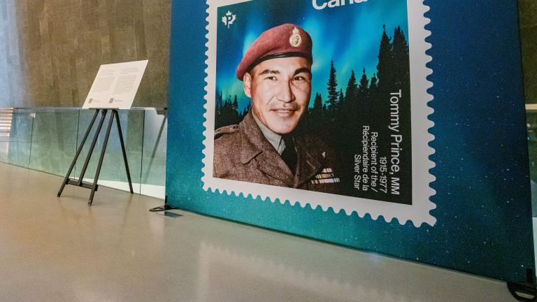 Un grand affichage d'un timbre représentant le sergent Tommy Prince est visible sur le côté droit de l'image. Une passerelle située devant le panneau d'affichage mène à gauche de l'image, dans la galerie Perspectives indigènes. Visibilité masquée.