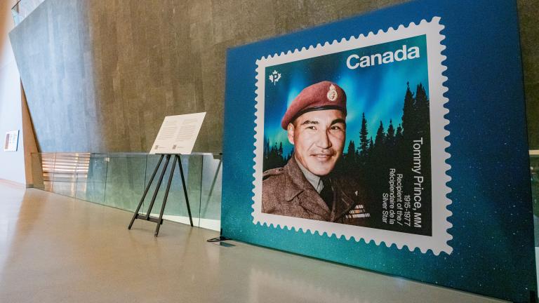 Un grand affichage d'un timbre représentant le sergent Tommy Prince est visible sur le côté droit de l'image. Une passerelle située devant le panneau d'affichage mène à gauche de l'image, dans la galerie Perspectives indigènes. Visibilité masquée.