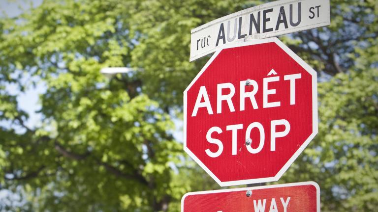 Un panneau d’arrêt et un panneau de signalisation de rue, en français et en anglais, se trouvent devant des arbres. Visibilité masquée.