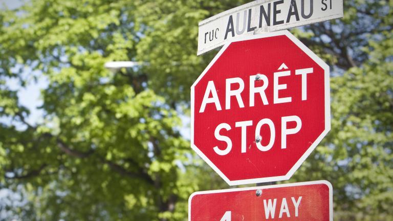 Un panneau d’arrêt et un panneau de signalisation de rue, en français et en anglais, se trouvent devant des arbres. Visibilité masquée.