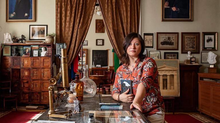 Une femme est à genoux près d’une table basse entourée de livres et d’objets de famille. Visibilité masquée.