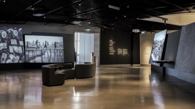  Une galerie de musée où on voit des photographies projetées sur de grands écrans. Il y a des fauteuils au milieu de la pièce.