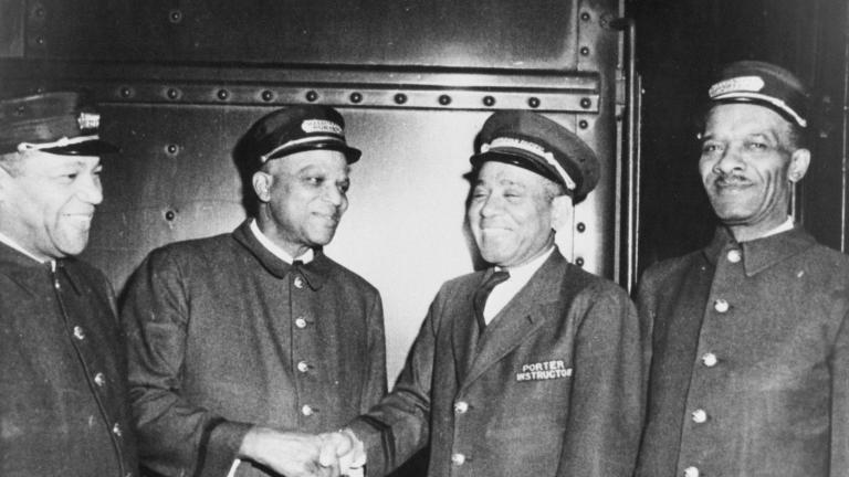 Photo en noir et blanc de quatre hommes en tenue de porteurs ferroviaires. Tous les quatre sourient et les deux du centre se serrent la main.