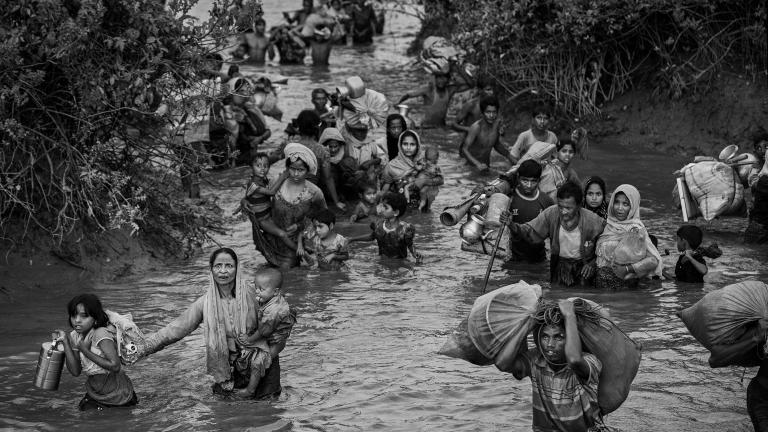 Des femmes, des enfants et des hommes rohingyas marchent dans l’eau d’une rivière qui leur monte jusqu’à la taille. Certaines personnes portent des jeunes enfants alors que d’autres portent des sacs de possessions, dont des articles ménagers.