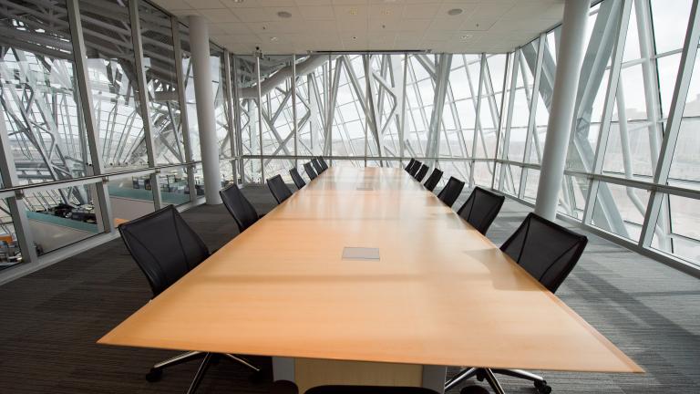 Une salle de réunion avec tapis, entourée de murs en verre, avec une longue table de réunion, des chaises et un écran de présentation.