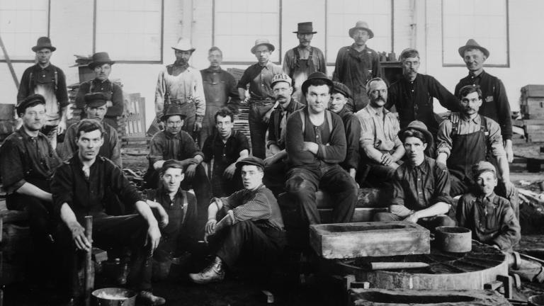 Un groupe d’hommes en vêtements de travail assis et debout dans une usine.
