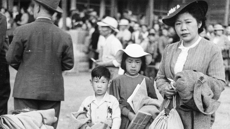 Photo en noir et blanc d’une femme avec deux enfants qui se tiennent derrière une pile de bagages et de couvertures et qui fixent l’objectif.