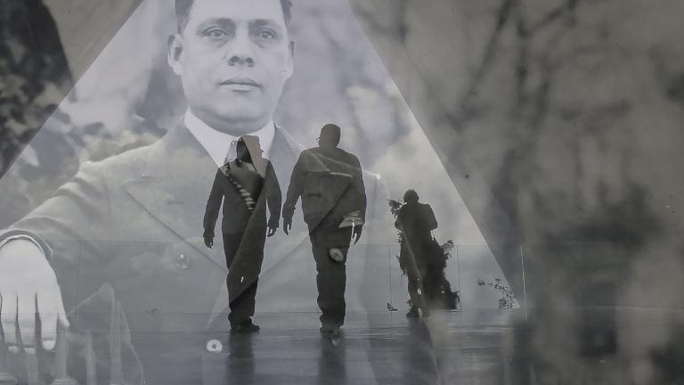 Une image historique translucide d’un homme en complet superposé à une photo contemporaine de deux hommes en silhouette marchant dans un corridor triangulaire. Visibilité masquée.
