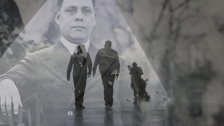 Une image historique translucide d’un homme en complet superposé à une photo contemporaine de deux hommes en silhouette marchant dans un corridor. Visibilité masquée.