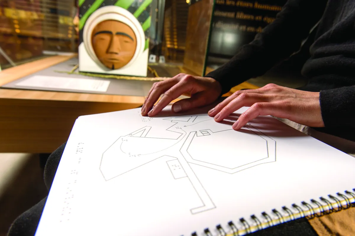 A person’s hands are reading braille on a page of a ring binder notebook with geometric designs.