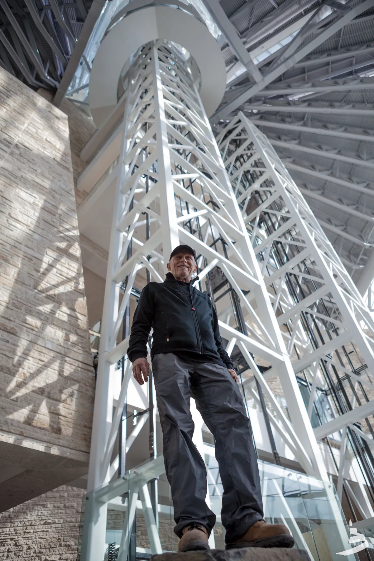 Antoine Predock, l'architecte du Musée, pris en photo en contre-plongée à l’intérieur du Musée. Des poutres blanches s’étendent vers le haut derrière lui.