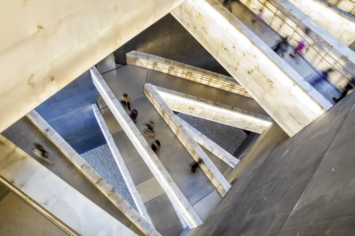 Vue en plongée des rampes en albâtre du Musée qui s’entrecroisent. On voit des gens marcher sur les rampes.