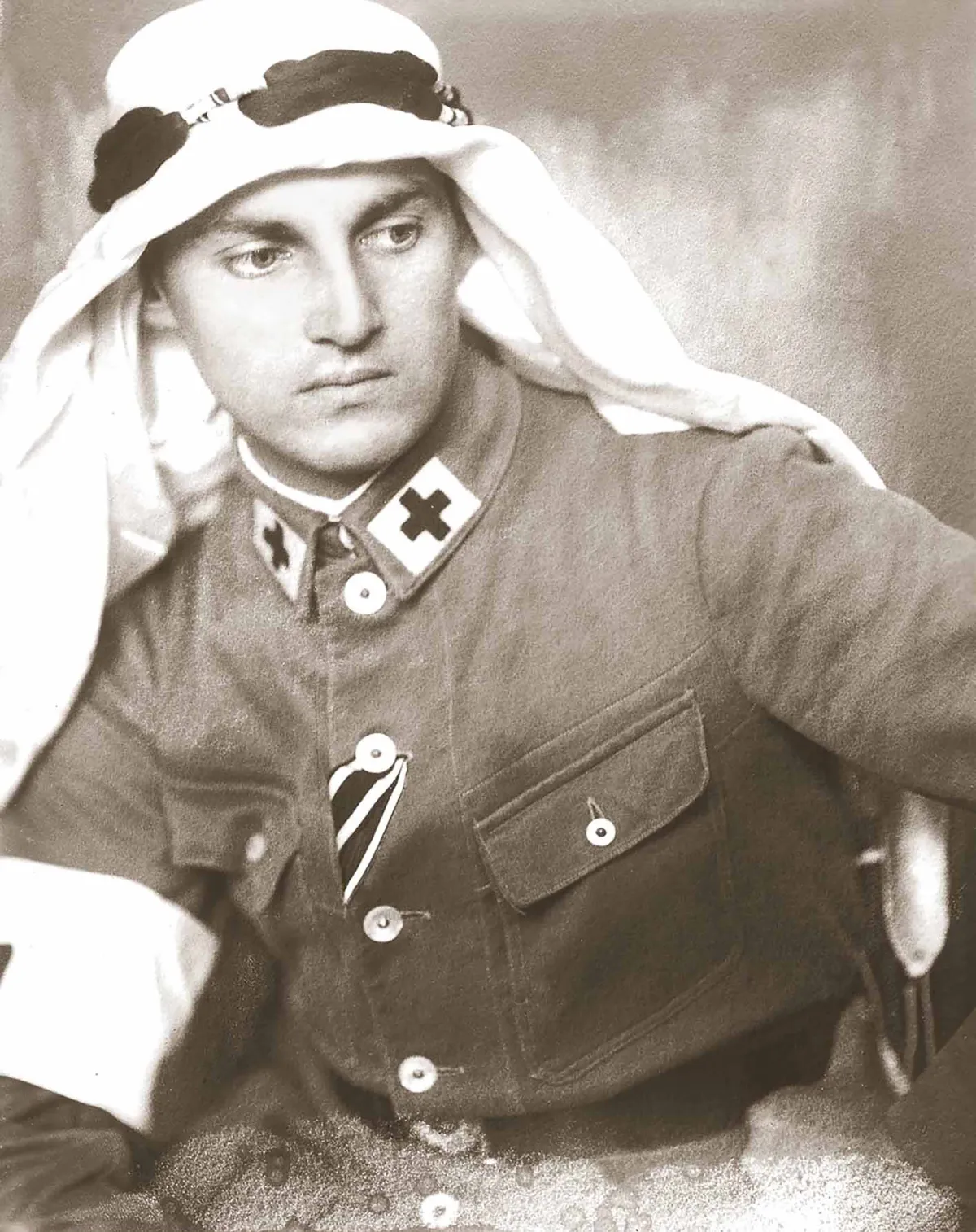 Un homme blanc en uniforme militaire avec une croix noire au bord du col porte un keffieh, une pièce en coton blanc portée au Moyen-Orient.