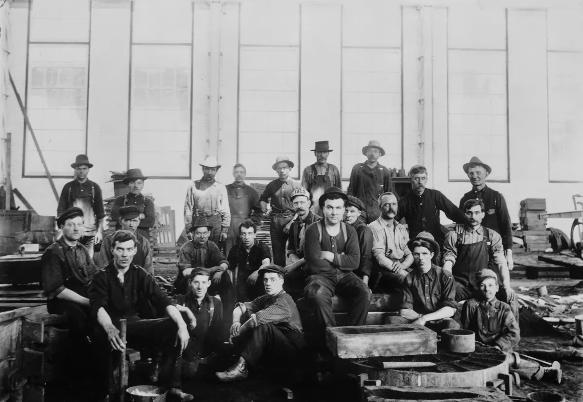 Un groupe d’hommes en vêtements de travail assis et debout dans une usine.