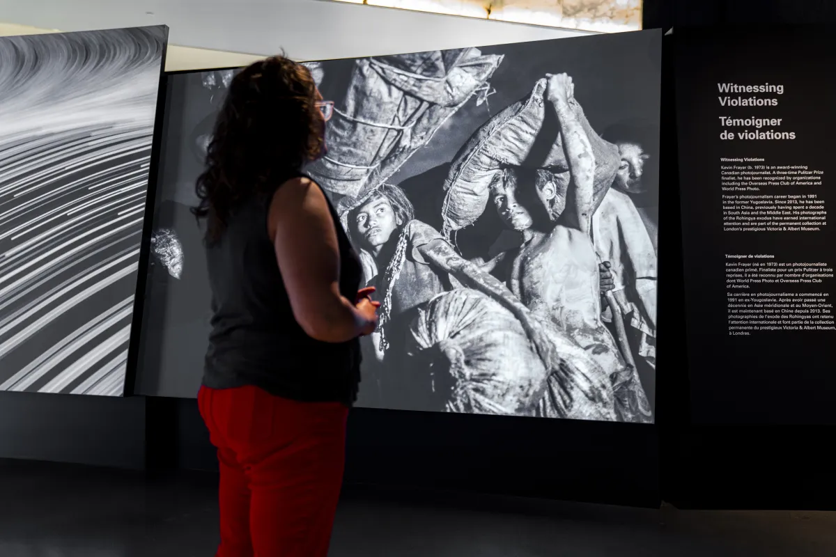 Une femme regarde une grande photo projetée. À côté, il y a un panneau de texte intitulé « Témoigner de violations ».