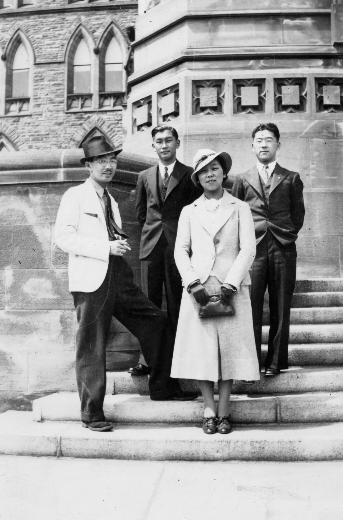 Une image en noir et blanc de trois hommes et d’une femme debout sur un escalier en pierre.