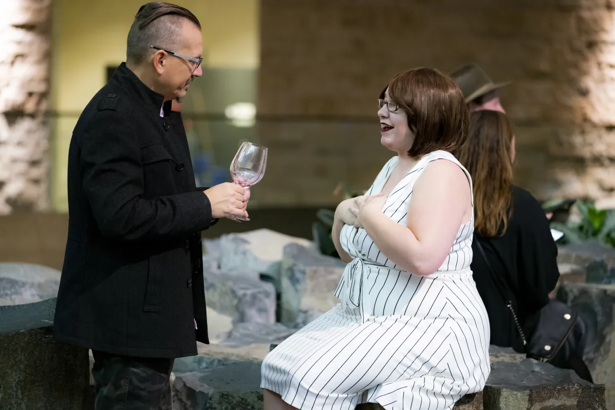 Un couple dans un espace du Musée. La femme est assise sur des piliers de roche. L’homme est debout, un verre de vin à la main.