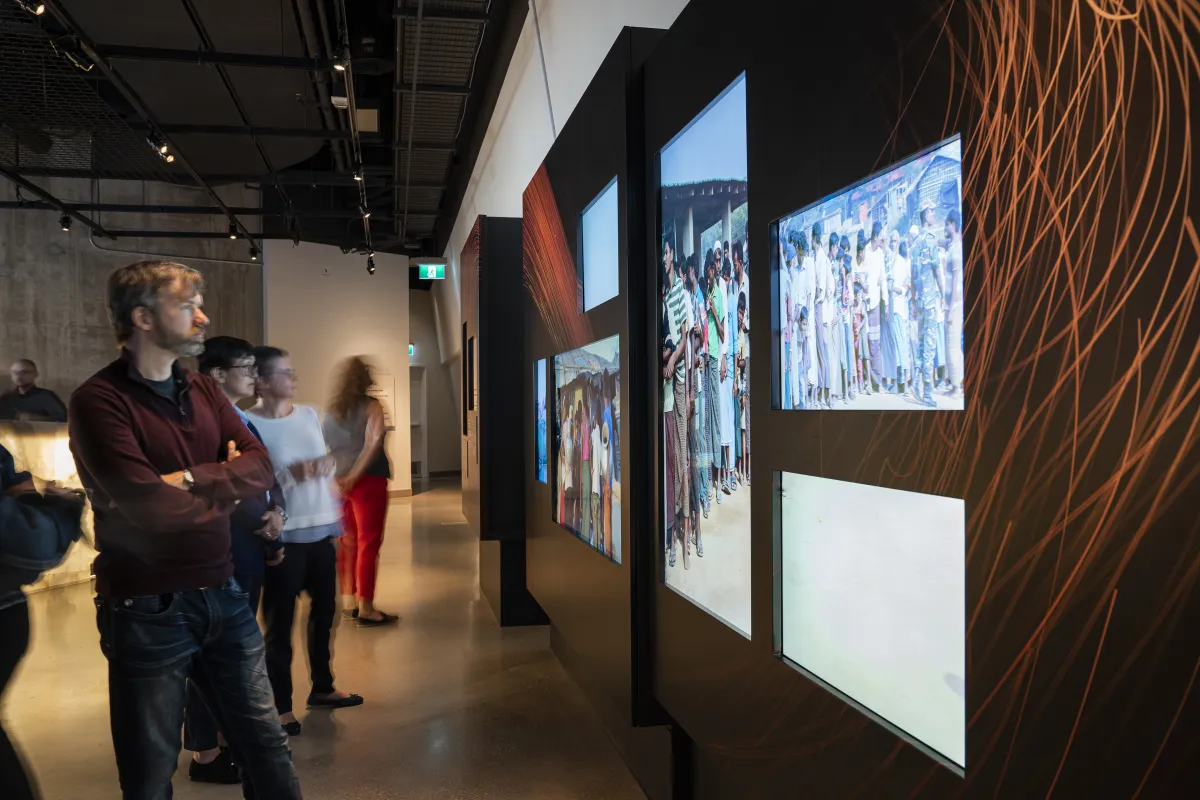Quelques personnes regardent une élément d'exposition comprenant des photographies numériques en couleur.