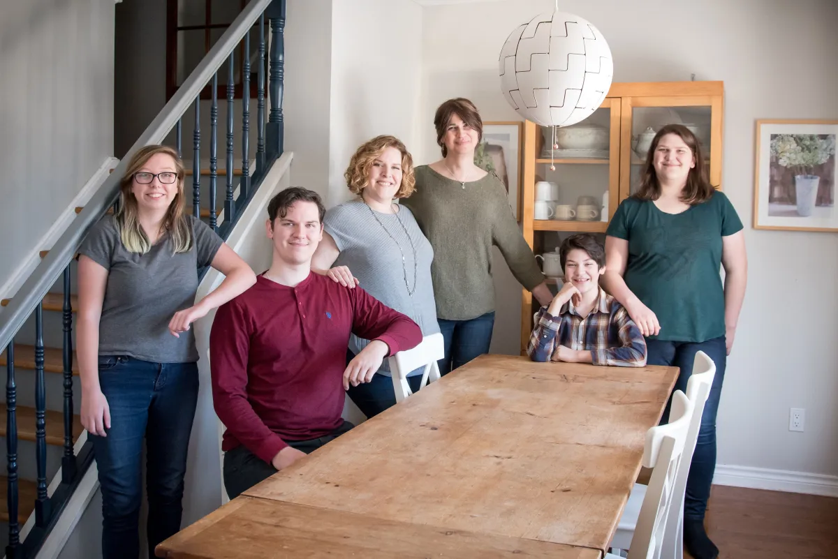 Une famille de six personnes souriantes rassemblées autour d’une table.
