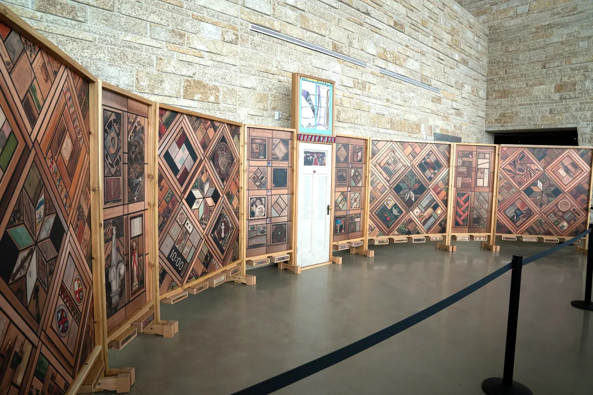 Vue de gauche d’une structure de panneaux de bois verticaux recouverts de motifs d’images, avec une porte blanche au centre.