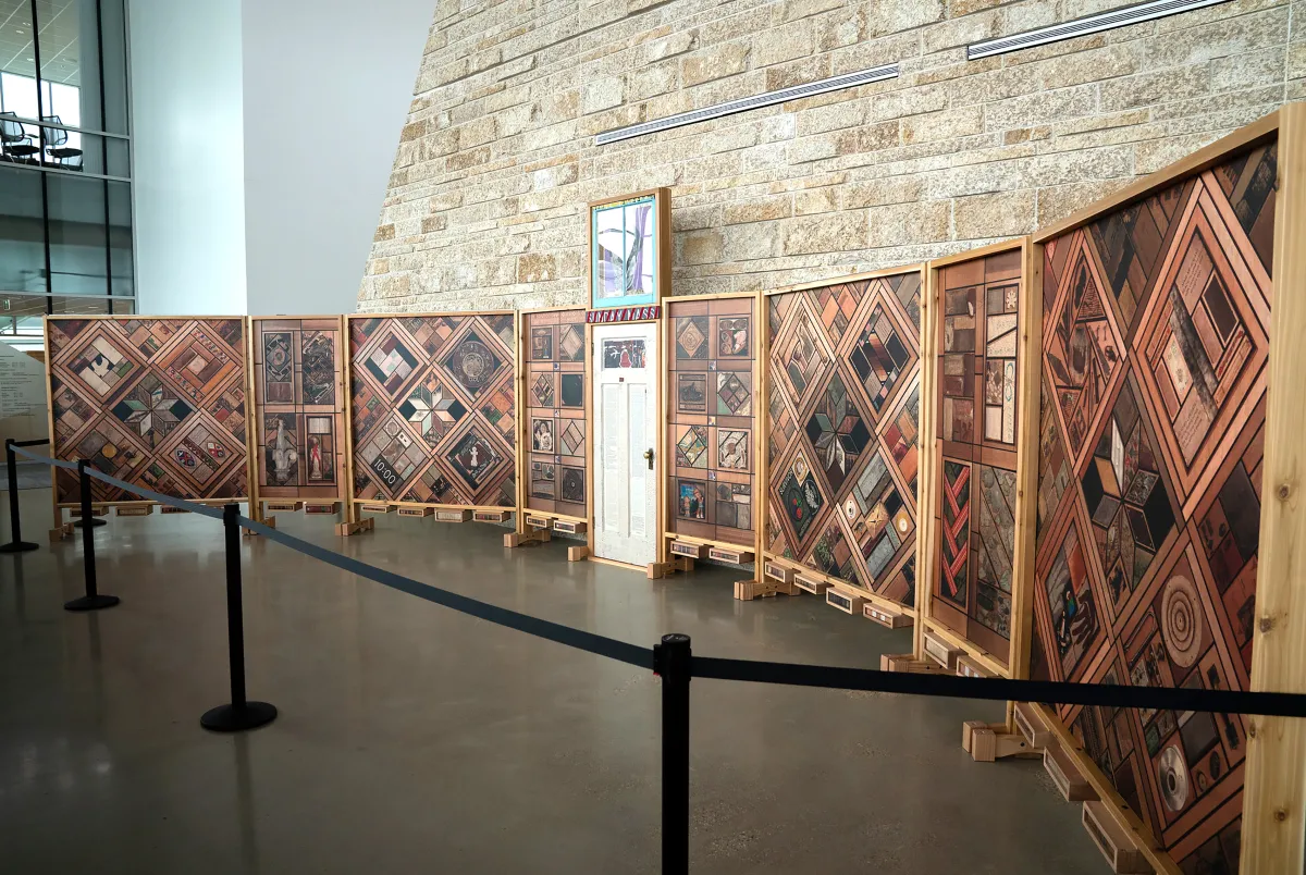 Vue de droite d’une structure de panneaux de bois verticaux recouverts de motifs d’images, avec une porte blanche au centre.