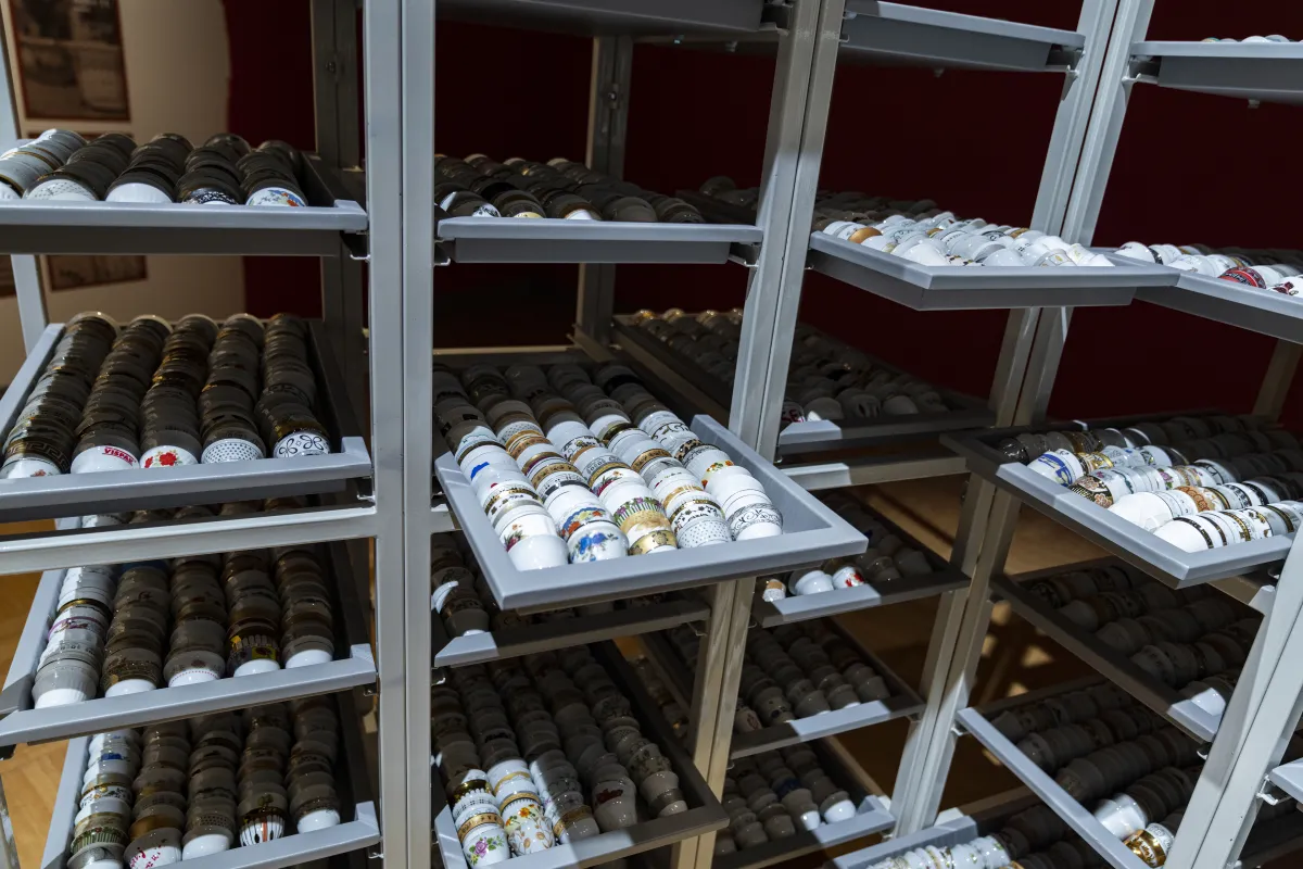 Des milliers de petites tasses en porcelaine sont disposées dans des plateaux sur un haut support métallique.