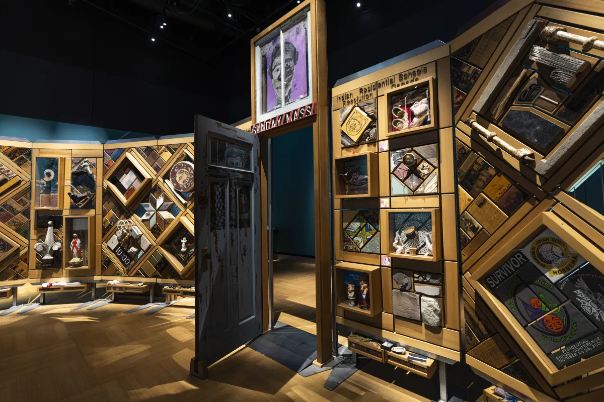 Une grande installation artistique autonome contient des centaines d’objets. Elle est encadrée de cèdre et il y a une porte ouverte au milieu que les gens peuvent franchir.