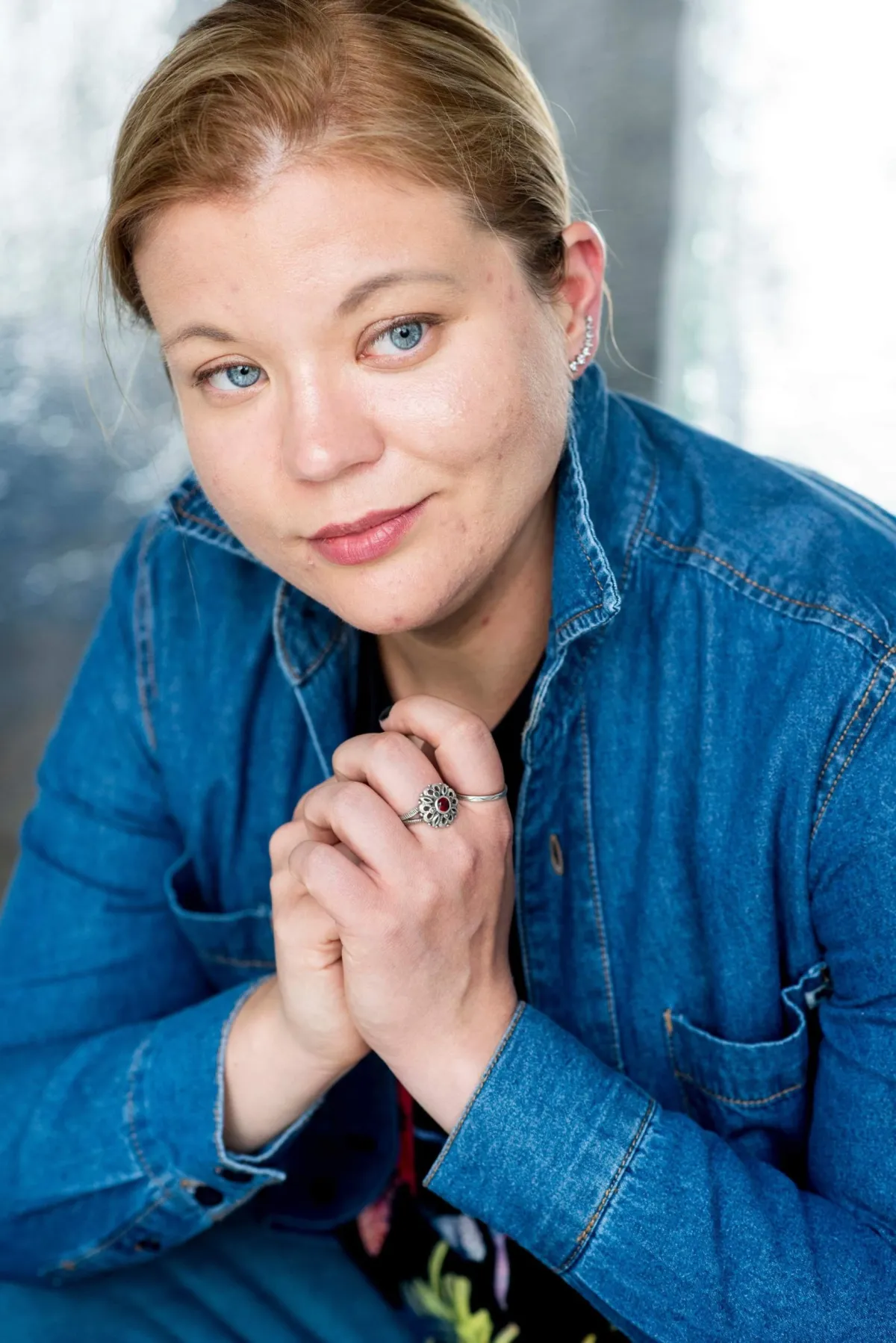 Geneva Halverson, une personne aux cheveux clairs et aux yeux bleus qui porte une chemise en jean bleu, se penche vers la caméra.
