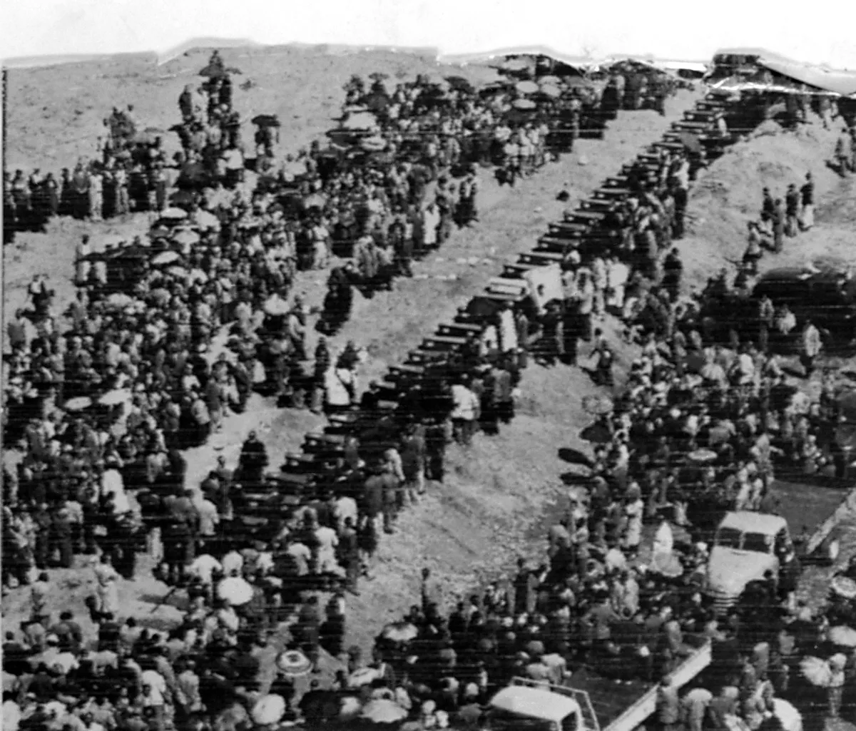 Photo aérienne d’une longue file de cercueils entourés d’une grande foule. 