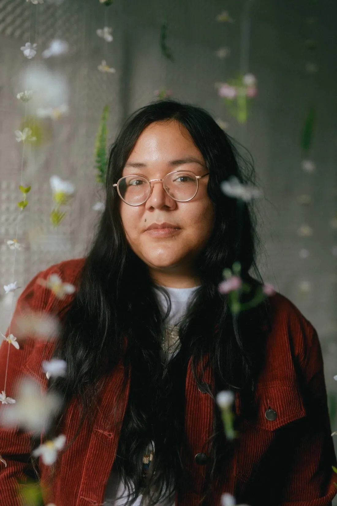 Veronica Blackhawk, une jeune Anishinaabe aux longs cheveux noirs et aux lunettes rondes, porte une veste en velours côtelé rouge.