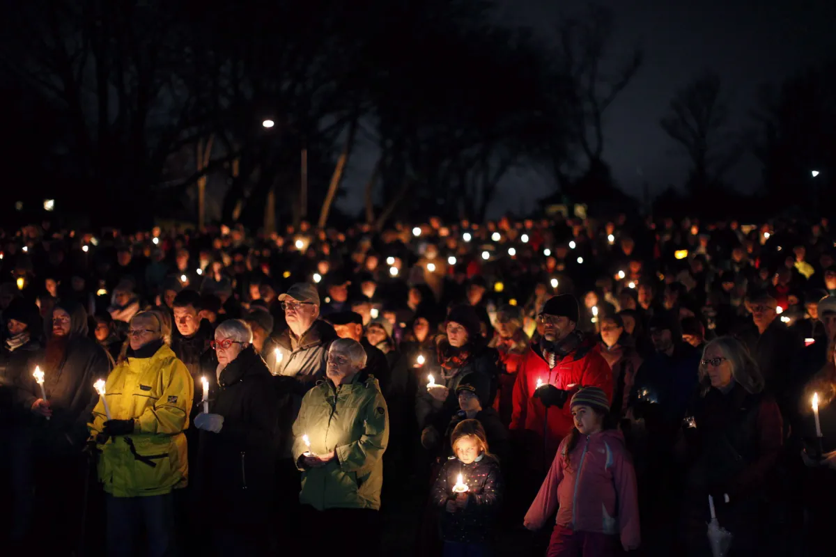 Une grande foule de personnes rassemblée à l’extérieur dans la nuit, tenant des bougies.
