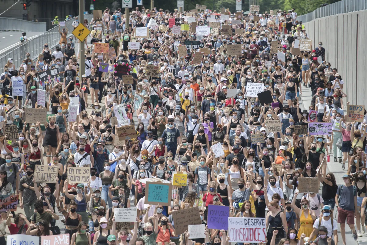 Une très grande foule de personnes marchant dans une rue large. Beaucoup portent des pancartes avec des slogans tels que « Don’t touch me », « Abusers deserve consequences » et « No means no ».