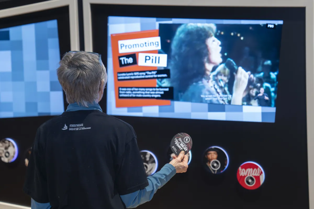 Une personne en visite utilise un disque contenant la technologie RFID pour interagir avec un écran montrant une chanteuse et un texte. Le titre en gros caractères en anglais dit : « Promouvoir la pilule ».