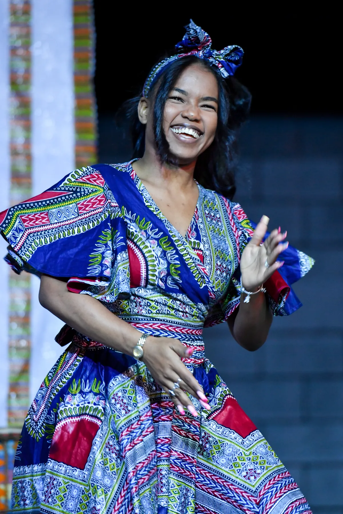 Une femme noire portant une robe africaine traditionnelle sourit tout en dansant.