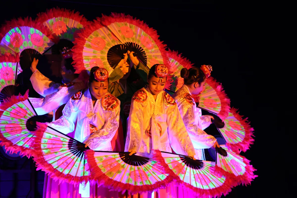 Des danseuses coréennes tenant de grands éventails ornés de fleurs sont regroupées de façon que leurs éventails forment un cercle.
