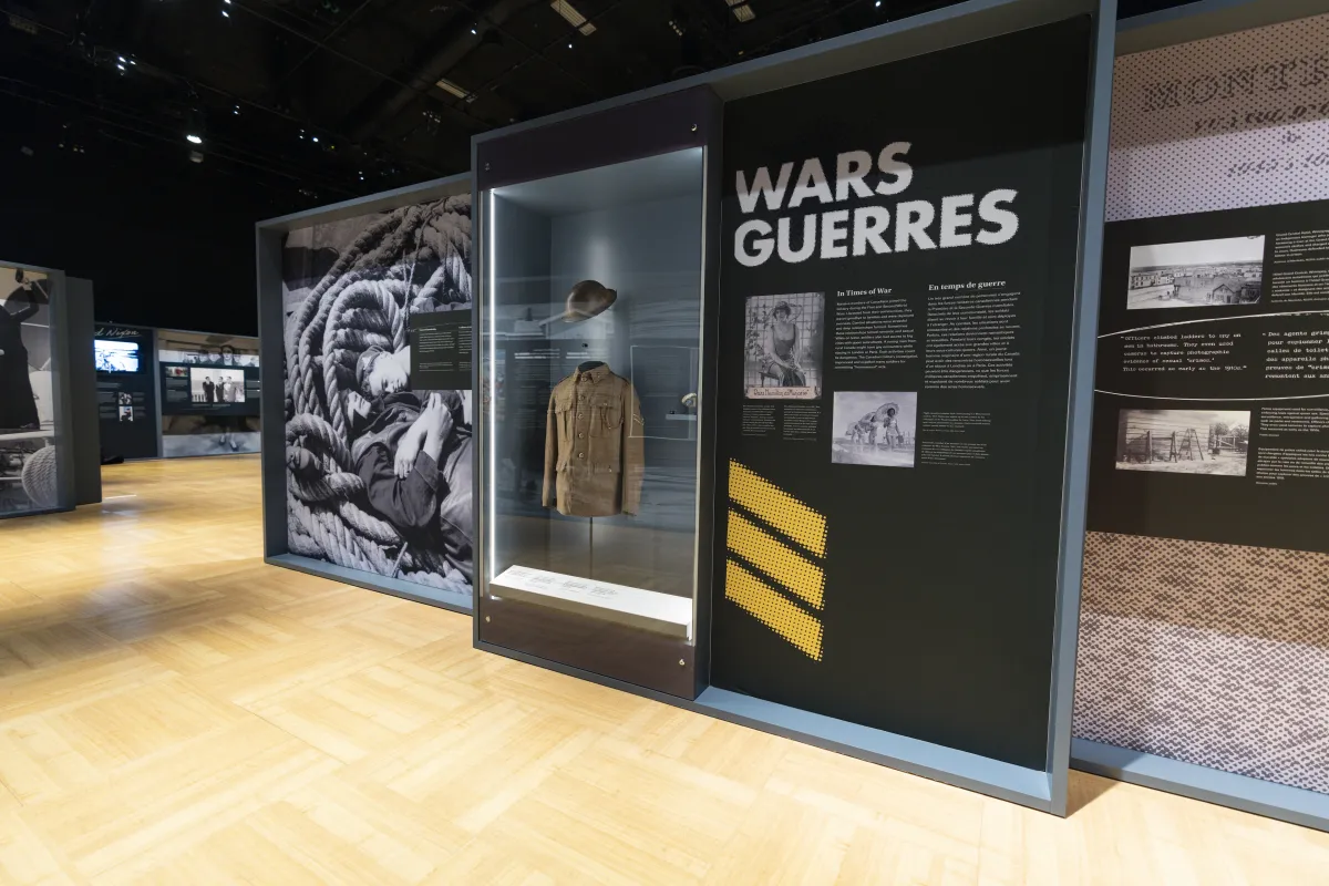 Une série de panneaux d’exposition présente des images historiques de militaires. Le mot « Guerres » figure en haut d’un des panneaux. Une vitrine située entre deux panneaux contient un uniforme militaire de la Première Guerre mondiale.