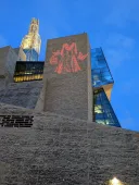 L’image d’une robe rouge flanquée de papillons rouges est projetée sur une façade en pierre calcaire à l’extérieur du Musée canadien pour les droits de la personne.