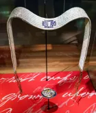 Une ceinture blanche et bleue faite de billes en coquillage est exposée sur un support.